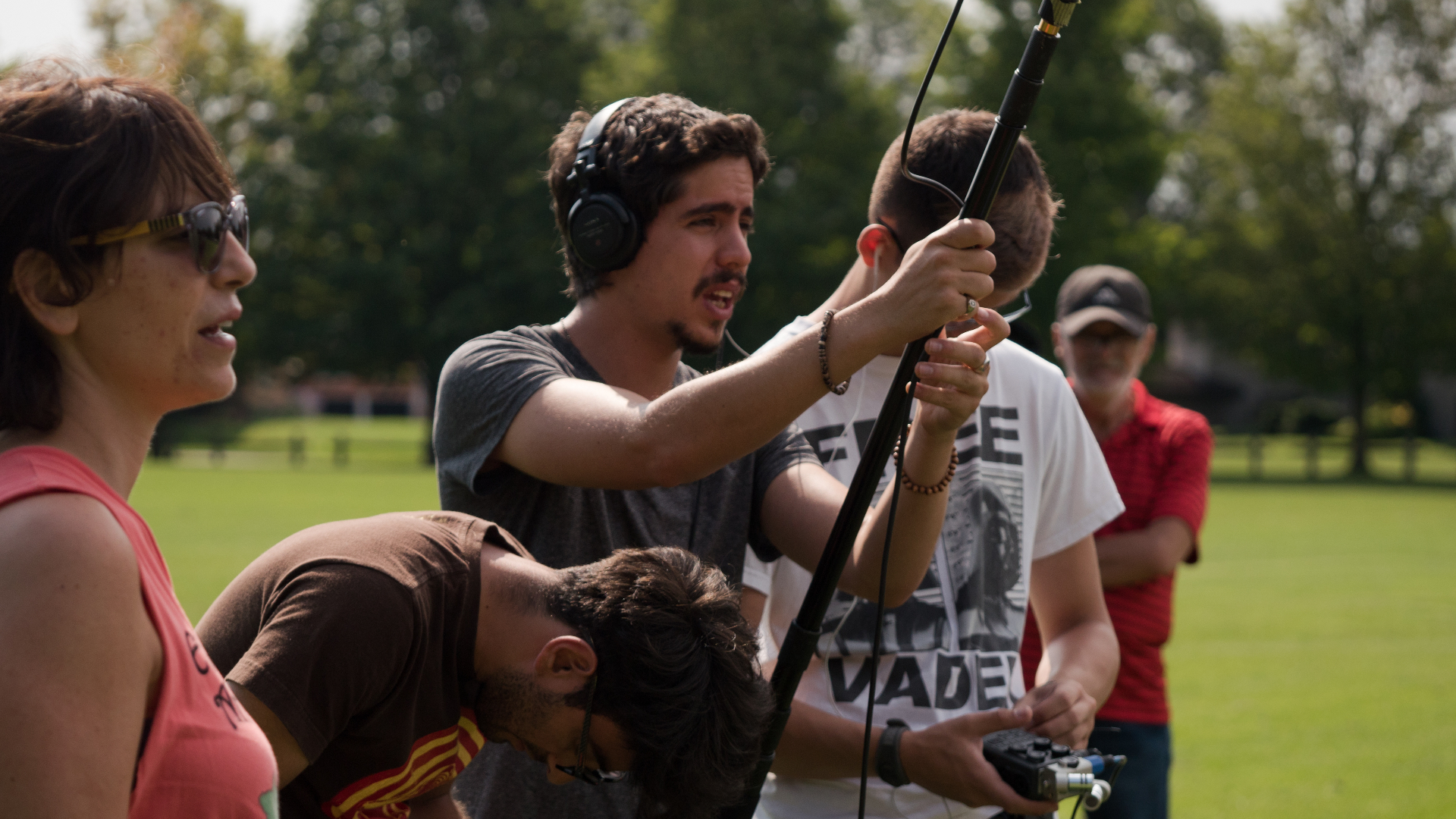 Andres boom-operating with headphones on a sunny exterior shoot.